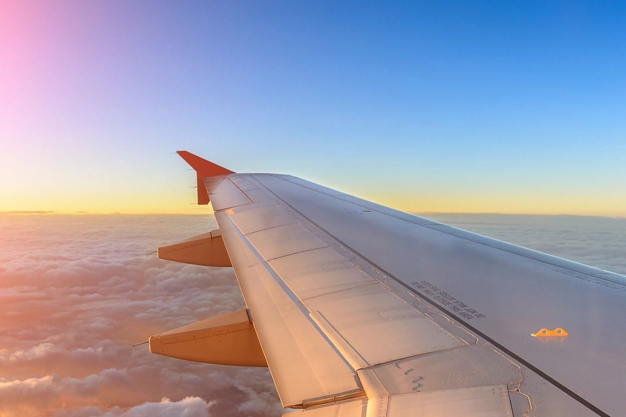 View of an airplane wing above clouds during a sunset flight.