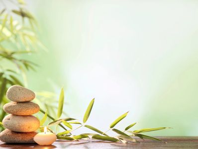 Stacked stones with a lit candle and bamboo leaves on wooden surface.