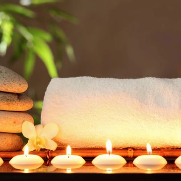 Peaceful scene with votive candles in the forefront and a rolled spa towel next to stacked stones