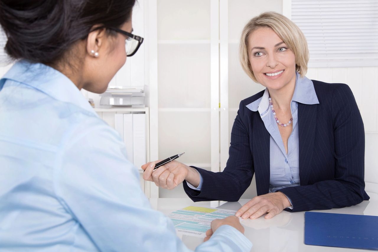 A real estate professional shares a positive report with her client at her desk.