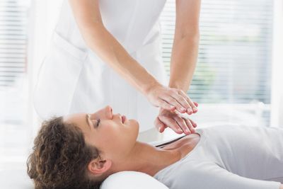 Young female woman receiving Reiki therapy on a white bed.