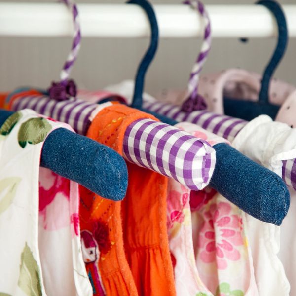 Colorful padded hangers holding floral and orange dresses on a clothing rack.