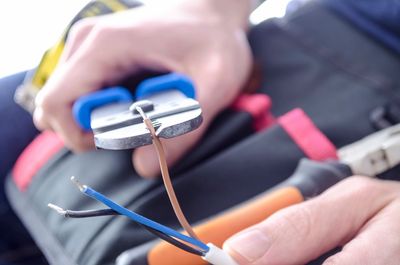 Cutting electrical wires with blue-handled wire cutters.