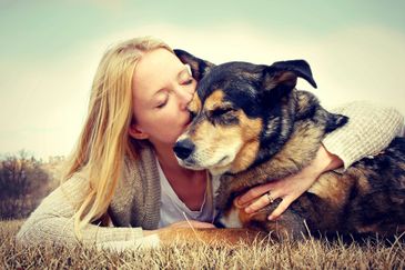 A woman lovingly kisses her large dog while lying on grass.