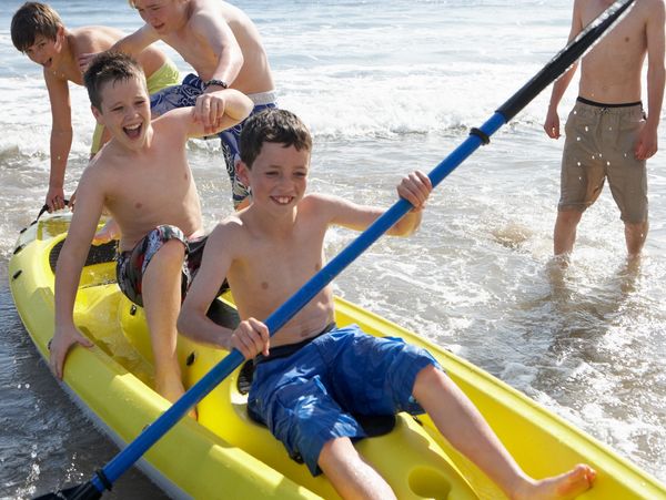 Boys kayaking in the small waves along the beach.