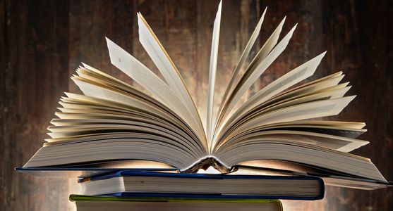 An open book with pages fanned out on top of two closed books.