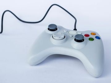 A white wired gaming controller on a white surface.