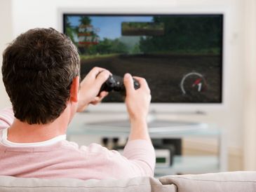 Man playing a racing video game on a TV from a couch.