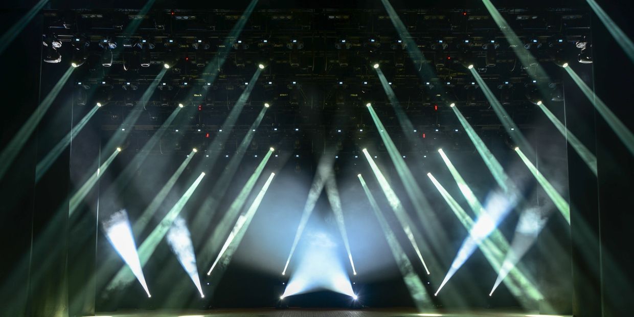 Bright stage lighting with multiple beams and smoke effects.
