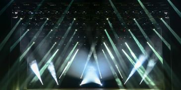 A dark stage illuminated by multiple bright spotlights and beams.