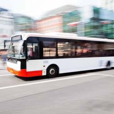 A city bus in motion with a blurred background showing urban buildings.