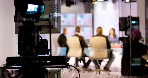 Professional video camera filming a panel discussion in a TV studio.