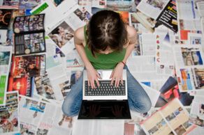 woman sitting on magazines on the floor typing on a laptop