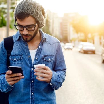 Man using phone while holding coffee outside.
