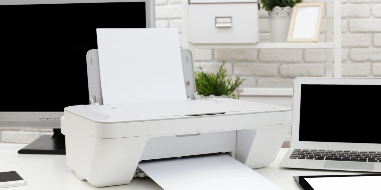 White printer printing paper on a modern office desk with computers.