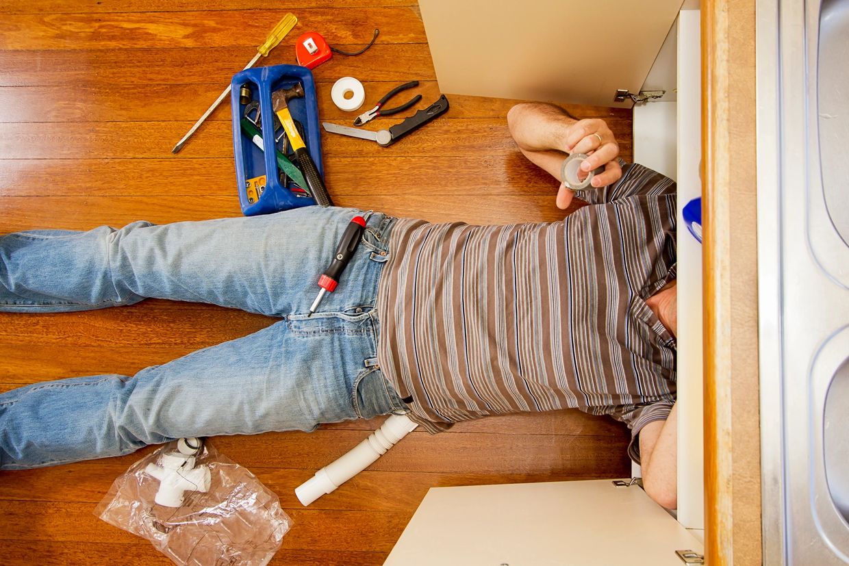 a plumber is fixing a leak under the bathroom basin