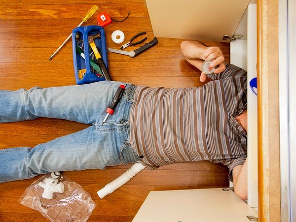 A man fixing plumbing under a kitchen sink with tools around him.