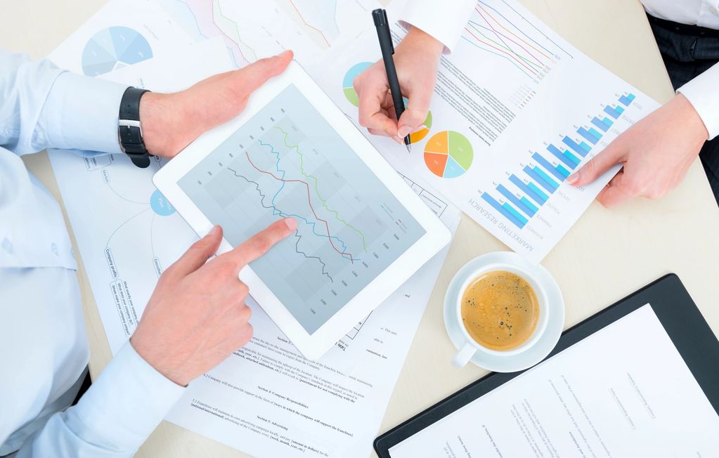 Two people analyzing financial charts with a tablet and printed graphs on a desk.