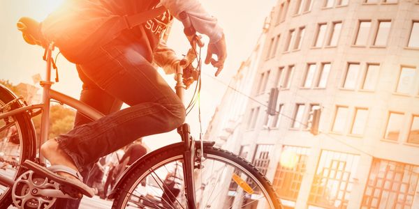 Persona montando bicicleta en la ciudad con luz solar intensa.