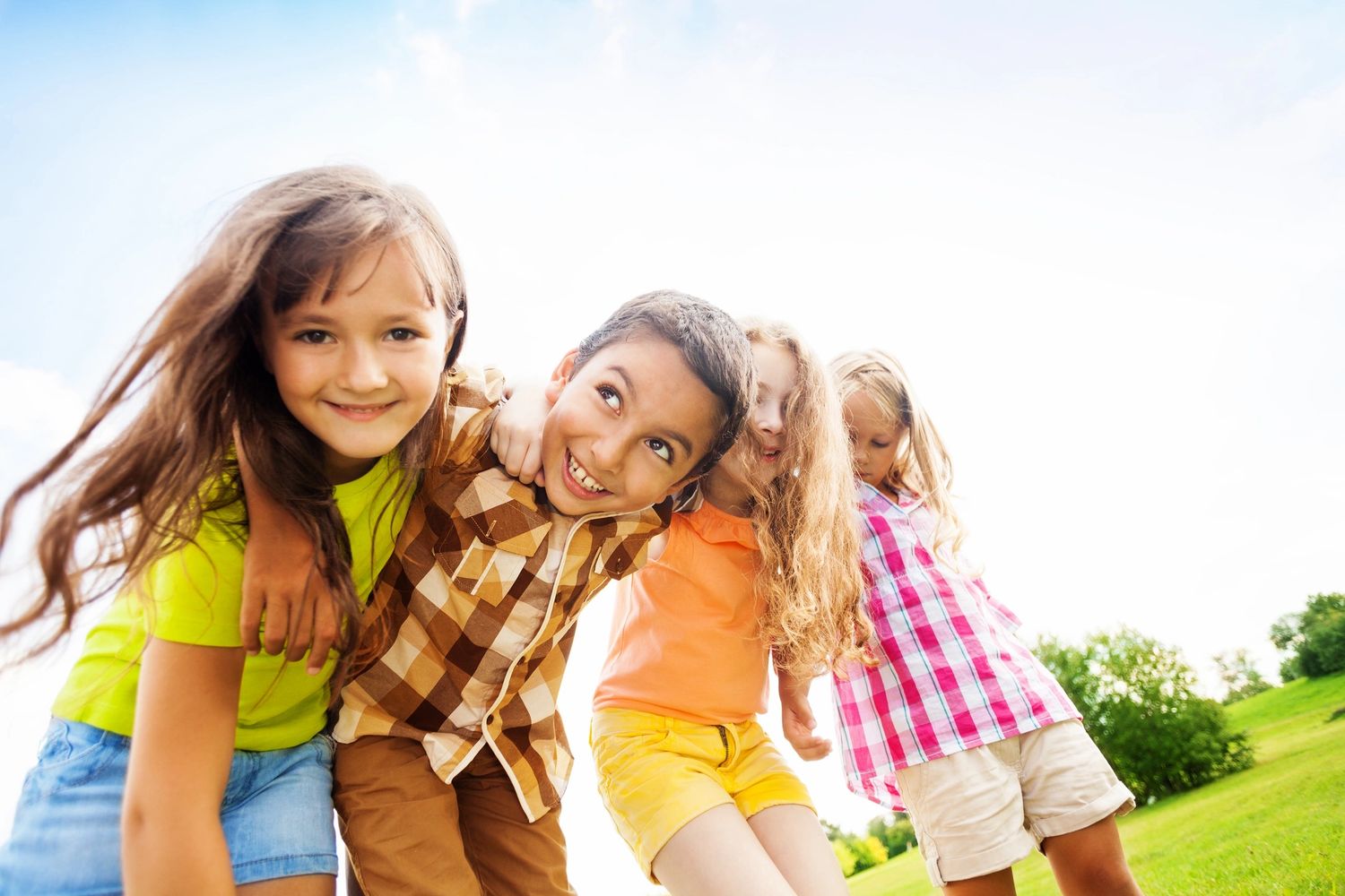 A group of children smile into the camera with their arms round their shoulders.