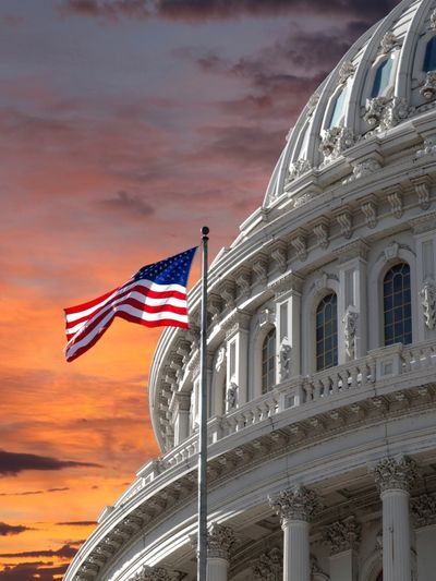 American flag waving near the U.S. Capitol dome at sunset.