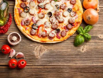 A delicious sausage and olive pizza with fresh ingredients on a wooden table.