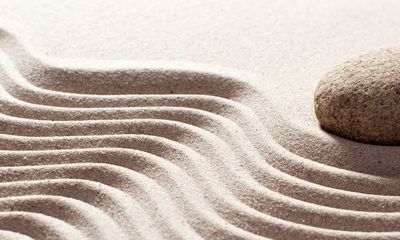 Peaceful rock sitting adjacent to sand carved with rippling waves, warmly basking in the sun