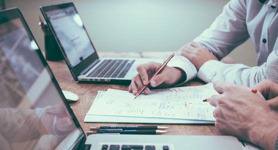 Two people collaborating with laptops and notes at a wooden table.