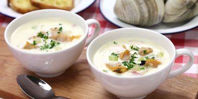 Two cups of creamy clam chowder garnished with herbs on a wooden board.