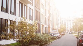 Sunlit residential street with parked cars and modern buildings.
