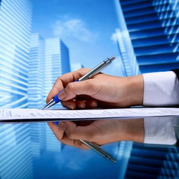 Hand signing a document with city buildings in the background.