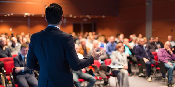 Image of a consultant leading a seminar with a large audience. 