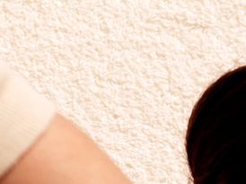 Close-up view of a textured beige wall with part of a light-colored sleeve and a dark circular.