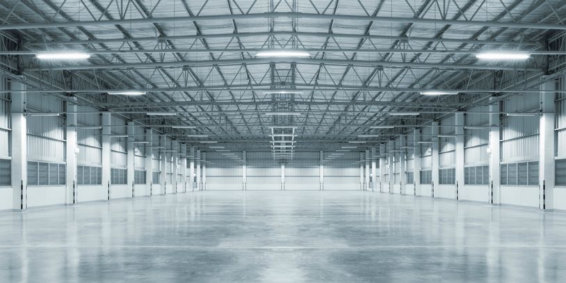 Spacious empty warehouse with polished concrete floor and metal roof structure.