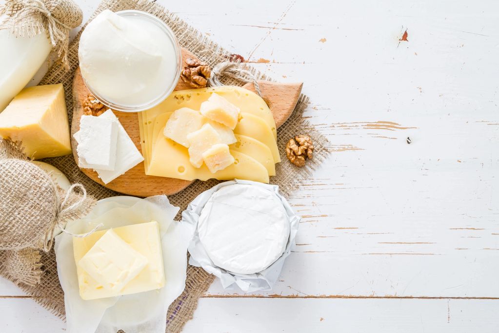 Variety of cheeses and dairy products on rustic wooden board.