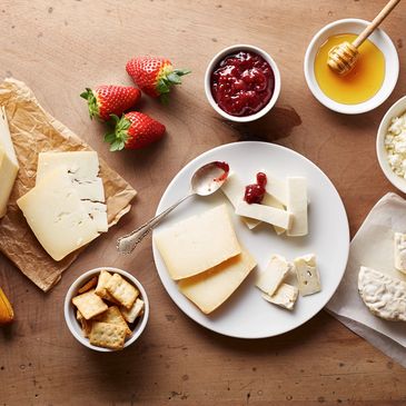 A cheese platter with strawberries, crackers, jam, honey, and cottage cheese.