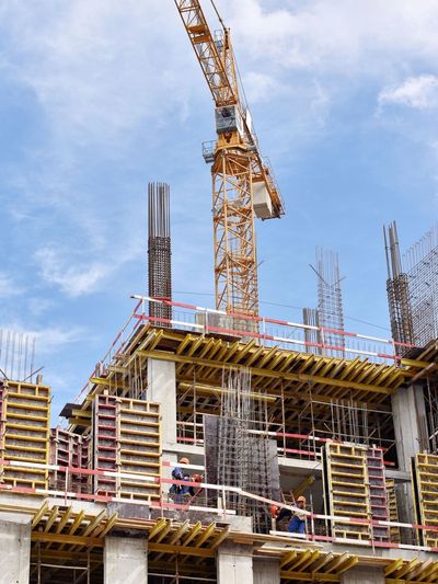 Construction site with workers and a tall crane against a blue sky.