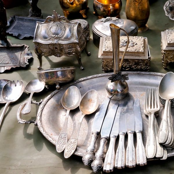A collection of vintage silverware and ornate metal containers arranged on a table.