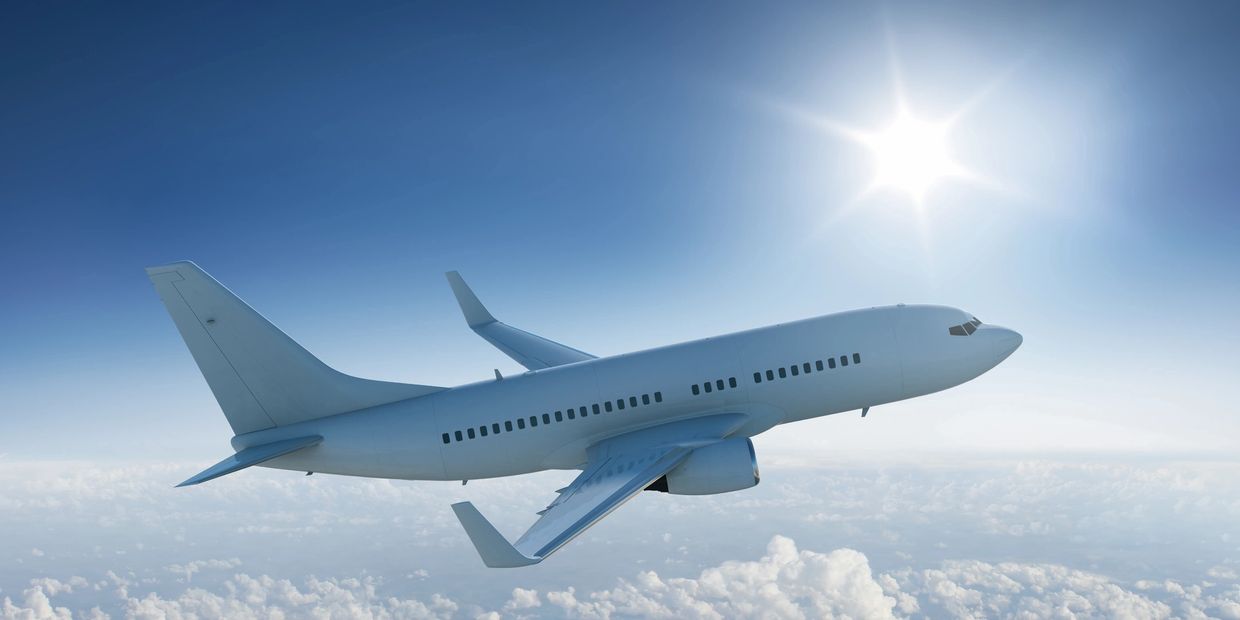 A white airplane flying above the clouds on a sunny day.