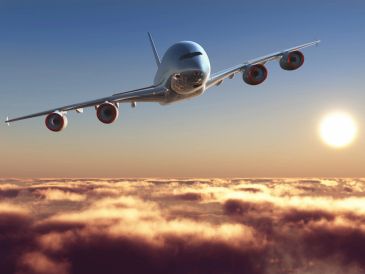 A large airplane flying above clouds at sunset.