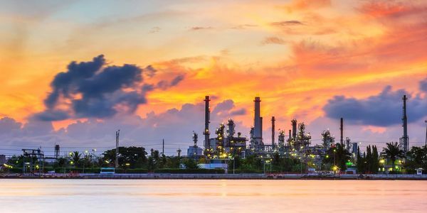 Oil refinery silhouette against a vibrant sunset sky by the water.