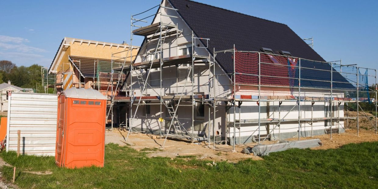 New houses under construction with scaffolding and a portable toilet nearby.
