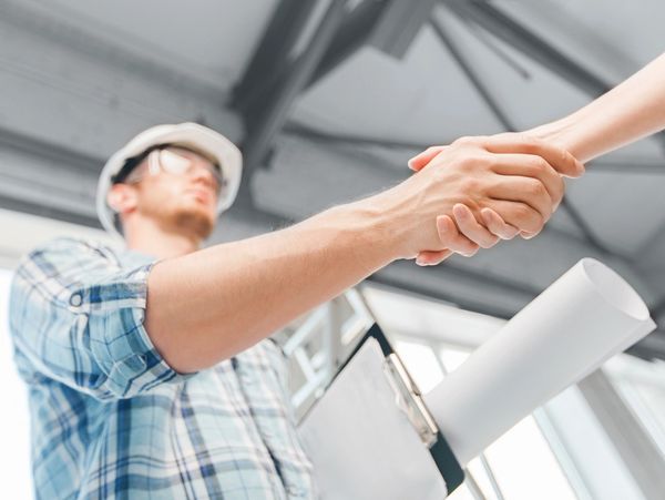 Man with hard hat and drawings under his arm shaking a person's hand