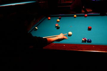 Person aiming to hit a ball on a pool table in a dimly lit room.