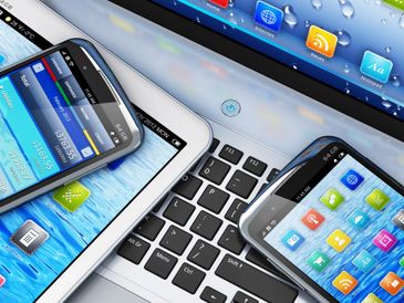 Multiple digital devices including smartphones, a tablet, and a laptop keyboard.