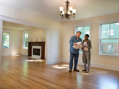 Two people reviewing plans inside an empty room with wooden floors. Calgary real estate neighborhood