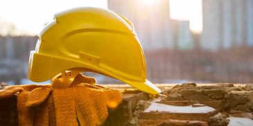 Yellow construction helmet and gloves on a brick wall at sunset.