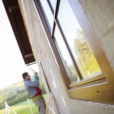 Worker applying sealant to an exterior window frame on a house.