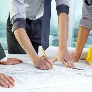 3 people surrounding a desk with construction plans