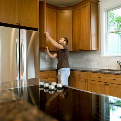 A person inspecting and cleaning an upper cabinet in a residential kitchen.